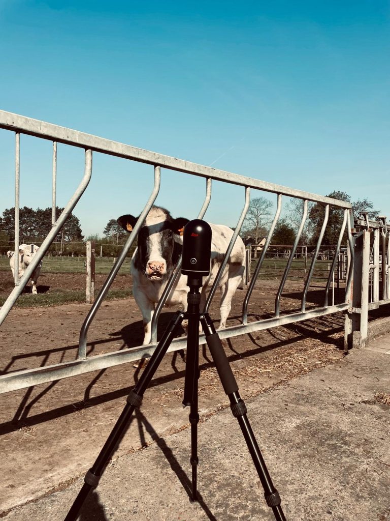 Landmeetapparatuur op statief in een open veld met ochtendzon en gebouw op de achtergrond